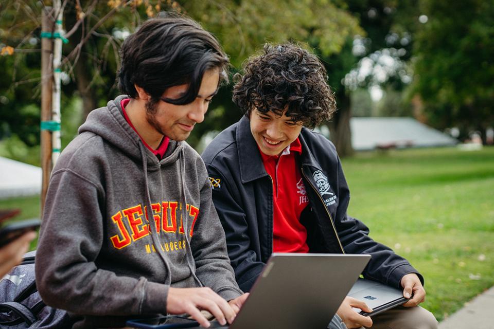 two students outside smiling at a laptop