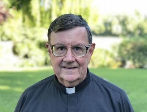 Image of Rev. Harris, S.J. on campus in front of garden