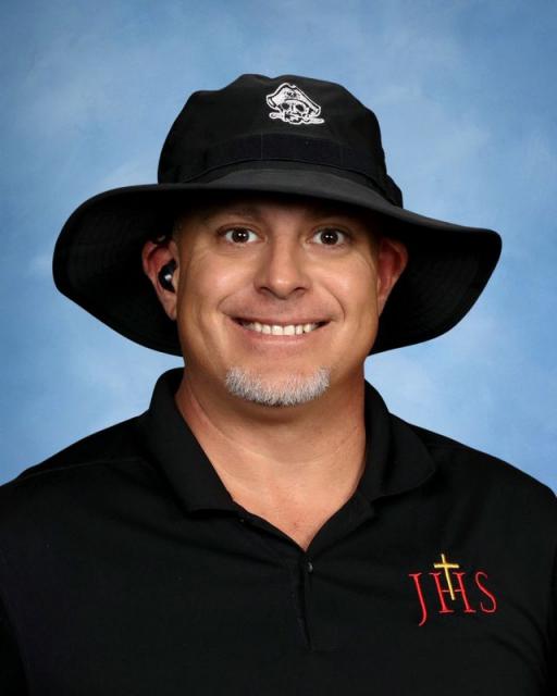 Studio head shot of Tony smiling and wearing a hat