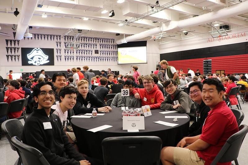 gym full of round tables with students, closest group is turned and smiling at camera