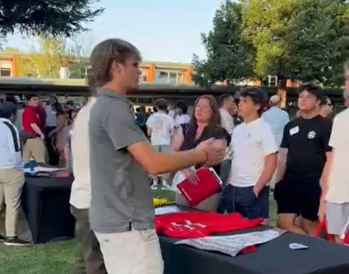 current student welcomes and speaks with the new incoming families at a table outside